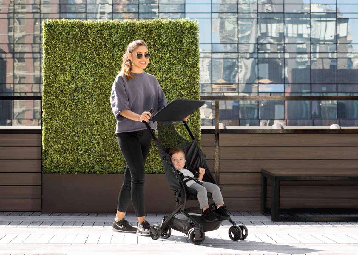 Caregiver pushing a toddler in The Clutch stroller in Black across an urban rooftop terrace, showing its compact one-seat frame in use