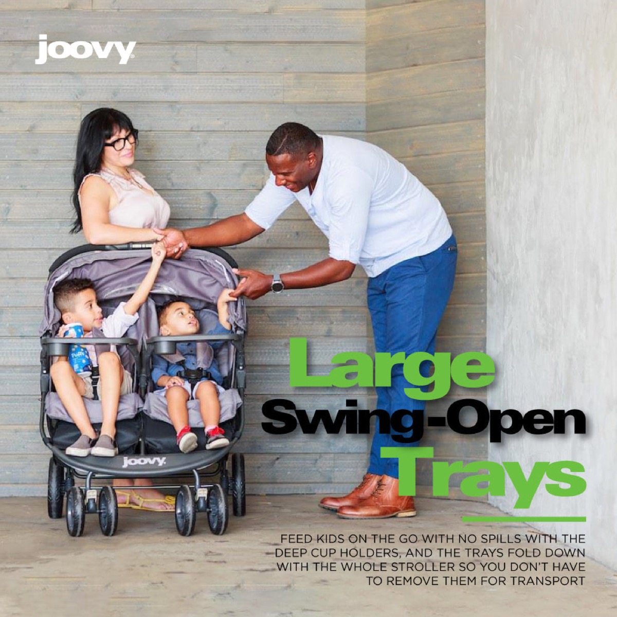 Official Joovy 'Large Swing-Open Trays' graphic: two children seated in the black Scooter X2 with trays and deep cup holders in use while parents lean in